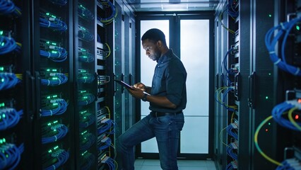 A man in jeans and a t-shirt stands in a server room, looking at a tablet. The scene conveys themes of technology, data management, and the digital age.