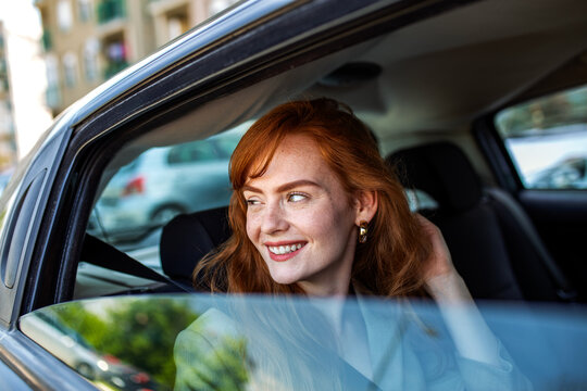 Smiling Redhead Woman Looking Out Car Window, Happy Female Passenger Enjoying the View, Young Ginger Girl Traveling by Car, Modern Lifestyle and Transportation Concept.