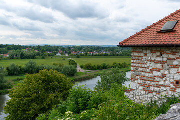 Obraz premium Elevated view of a winding river flowing through green meadows and rural landscape beside a historic stone structure. Scenic countryside panorama with dramatic clouds and distant village rooftops, ide