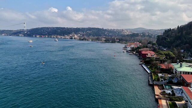 Aerial drone footage of the Kandilli and Vanikoy waterfront along the Bosphorus in Istanbul, showing coastal mansions, blue water, the bridge and hillside residences across the strait in a scenic view