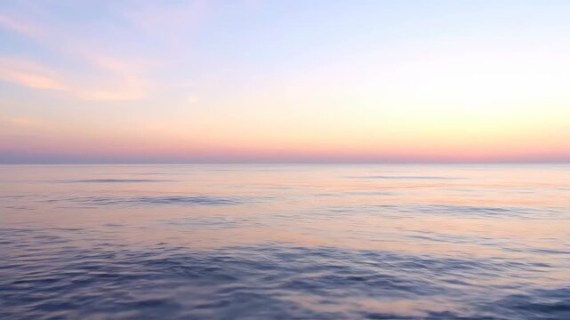 A serene seascape shows a gradient sky reflecting on tranquil water with gentle waves. The colors range from pale blues to warm sunset hues