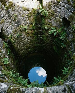Deep stone well surrounded by foliage reflecting sky on World Water Day  