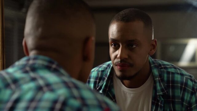 Gay man with lipstick reflected in the mirror and staring himself at dark room.
