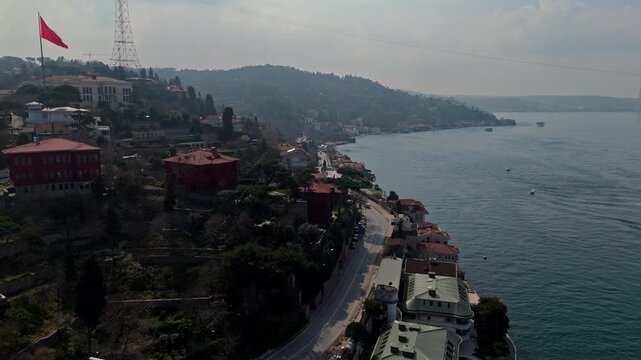 Aerial drone footage of the Kandilli and Vanikoy coastline along the Bosphorus in Istanbul, showing mansions, hillside residences, coastal road, blue waters and the large Turkish flag overlooking the 