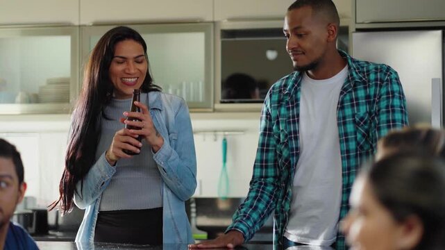Diverse group of happy male and transgender female friends drinking beer, cheering in living room. friends hanging out at home enjoying leisure time together.
