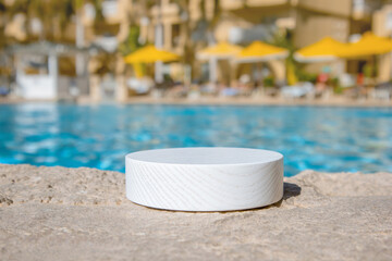 White wooden platform by a blue swimming pool, with defocused hotel yellow parasols and sun loungers in the background. Ideal as a product background, with lot copy space and a soft, blurred backdrop.