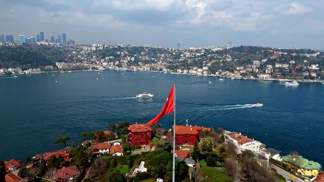 Aerial drone footage showing the large Turkish flag in Kandilli overlooking the Bosphorus, with red-roof homes, waterfront residences and the deep blue strait creating a striking coastal landscape.