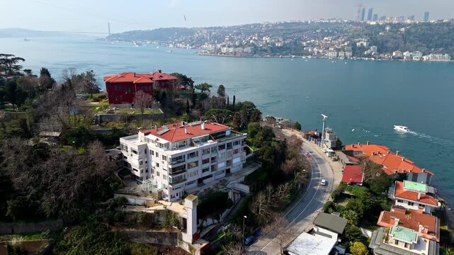 Aerial drone footage of the Kandilli and Vanikoy coastline along the Bosphorus in Istanbul, showing hillside homes, coastal roads, lush greenery and the large Turkish flag overlooking the waterfront l