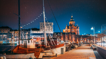 Helsinki, Finland. Pier With Boats, Pohjoisranta Street And View Of Uspenski Cathedral In Evening Night Illuminations. Night stars shining above street