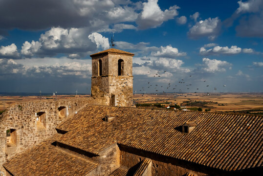 Dramatic view of an ancient abandoned church tower rising from terracotta-tiled ruins against a vast, open meseta landscape in Castilla-La Mancha, Spain. Dramatic blue sky with fluffy white clouds, go