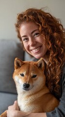Young woman with curly red hair and freckles smiling while holding a cute shiba inu dog, representing pet ownership, companionship, happiness, and the bond between humans and animals