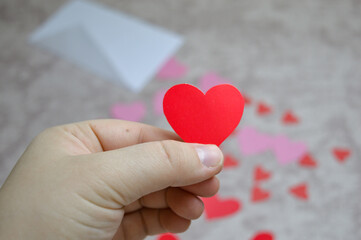 Fototapeta premium hand holding red paper heart with envelope and hearts in background, valentine’s day love message concept for romantic greeting cards, dating, relationships, wedding and holiday marketing