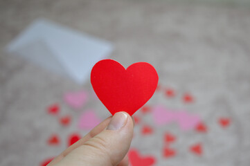 Fototapeta premium hand holding red paper heart with envelope and hearts in background, valentine’s day love message concept for romantic greeting cards, dating, relationships, wedding and holiday marketing