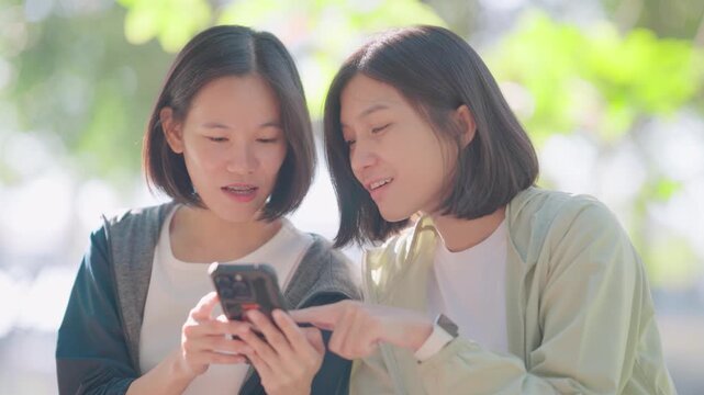 Group of sporty girlfriends relaxing under a tree and checking social media on mobile phones. They show healthy meal pictures to each other to discuss nutrition after exercising outdoors