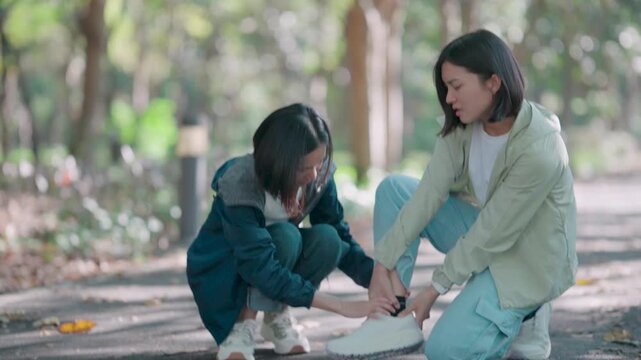 Two exhausted female runners helping each other treat a sprained ankle in the park. One friend massages the painful leg of the other after a running accident to provide immediate relief and care.