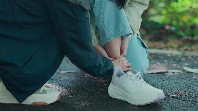 Caring female friend massaging the injured foot of a runner who sprained her ankle. Two tired women support each other after an accident during their morning exercise routine in the public park.