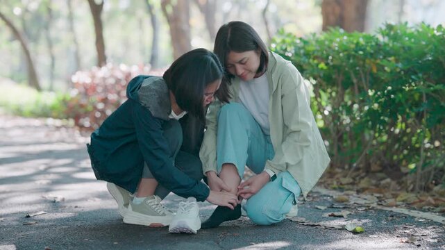 Health concept where two women treat a sports injury outdoors. A friend applies first aid massage to a painful sprained ankle after running ensuring safety and recovery for the tired athlete now.