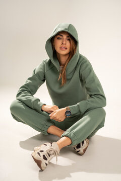 Confident young woman wearing a mint athleisure set with sweatshirt and sweatpants, posing in a minimal studio on a light background. Modern casual fashion, comfort wear, sporty lifestyle