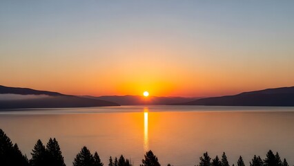 Sunset over tranquil lake with glowing sky pine tree silhouettes and mountain shadows in peaceful dusk