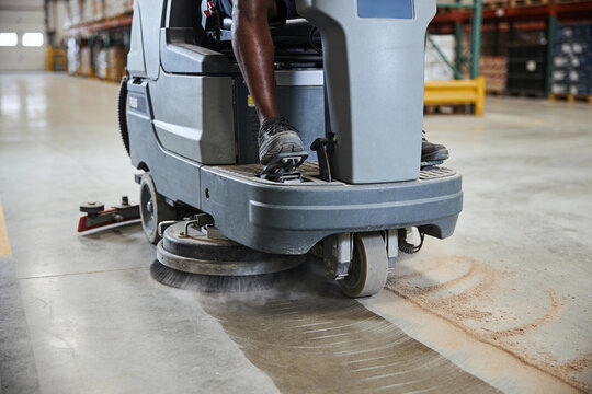 Industrial floor scrubber machine cleaning a warehouse concrete floor with spinning brushes
