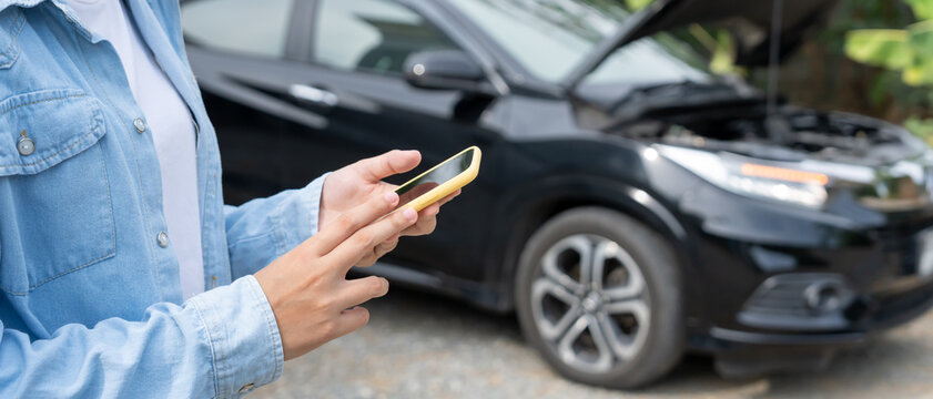 breakdown, broken car, repair. Woman uses mobile phone check insurance premiums through application due to car accident . Find garage to get car fixed during country tour, waiting for help, emergency.