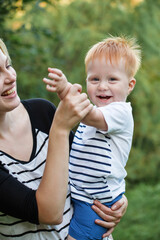 Mom and son are playing together outdoors in the summer. Mother is holding the kid boy