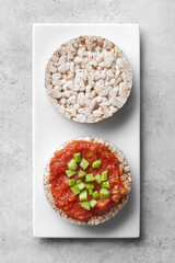 Puffed rice cakes with tomato paste and celery on a white plate, grey background. Top view