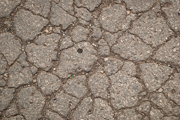Fototapeta premium Detailed close-up of cracked asphalt road surface with rough stone texture. Urban pavement background showing wear, damage, and aging construction material.