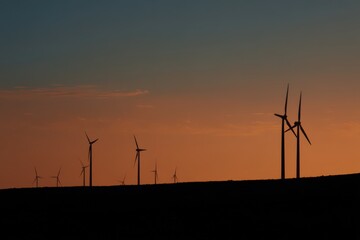 Sunset view of wind turbines silhouetted against a colorful sky over a rural landscape with rolling hills and open fields