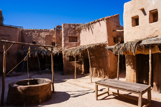 Rustic village scene under clear blue sky with stone buildings and straw-covered structures. Ouarzazate, Morocco