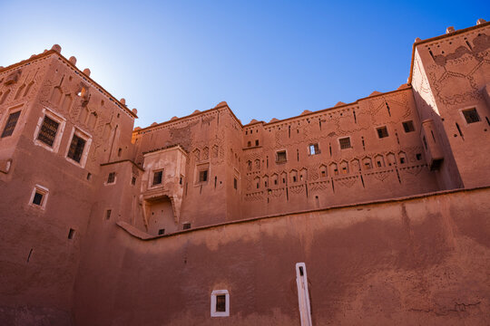 Sunlit ancient clay fortress with decorative patterns against a clear blue sky. Ouarzazate, Morocco