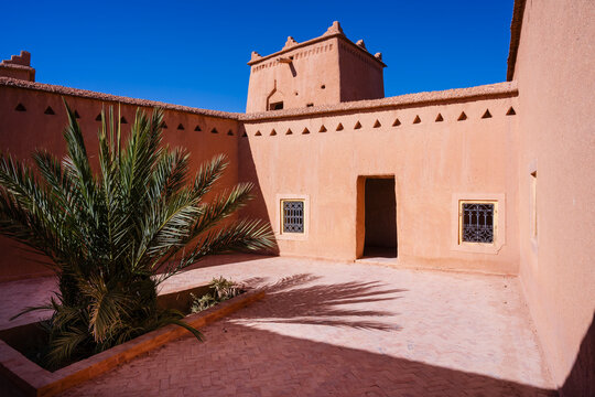 A sunlit courtyard with a palm tree and adobe walls under a clear blue sky. Ouarzazate, Morocco