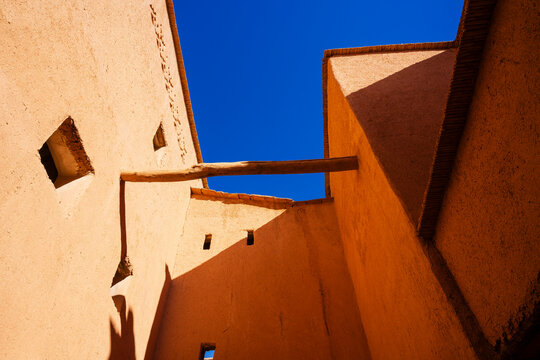 Sunlit clay buildings with wooden beam and windows against a clear blue sky. Ouarzazate, Morocco