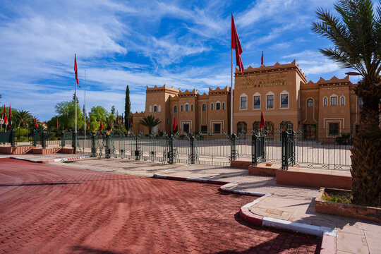 Ornate building with flags, palm trees, and blue sky in a sunny outdoor setting.   Ouarzazate, Morocco