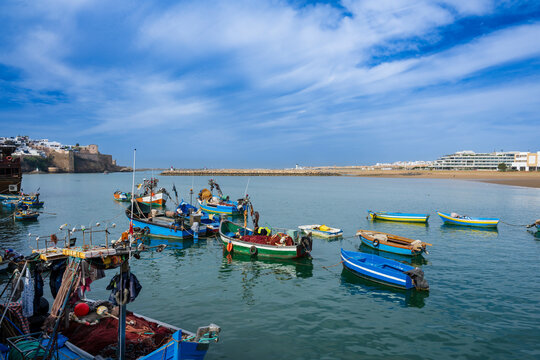 Colorful fishing boats float on a calm blue sea under a vibrant sky near a coastal town. Rabat, Morocco