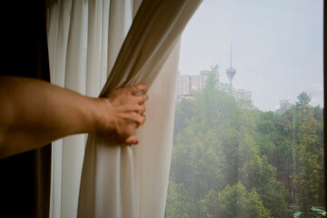 Hand opening curtain to reveal cityscape with tower and lush green trees. Chengdu, Sichuan, China