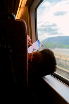 Person lying on train seat using a smartphone by the window with scenic view outside. Chengdu, Sichuan, China