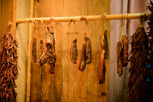 Cured meats and sausages hang from a wooden rod in a rustic setting. Chengdu, Sichuan, China