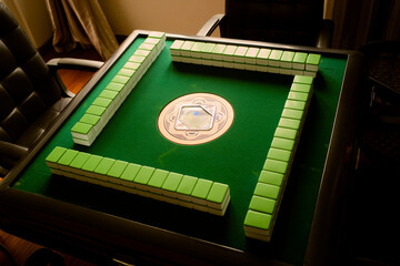 Green mahjong table with neatly arranged mahjong tiles and leather chairs in dim lighting. Chengdu, Sichuan, China
