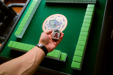 Hand holding a Mahjong tile with a green game table setup in the background. Chengdu, Sichuan, China