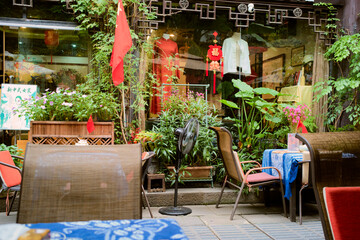 Outdoor cafÈ seating with lush plants, colorful tablecloths, and a fan in an urban setting. Chengdu, Sichuan, China