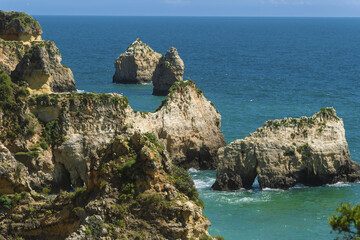 Coastal landscape in Portimão, Portugal featuring rugged limestone cliffs with patches of green vegetation and dramatic rock formations rising from turquoise sea waters