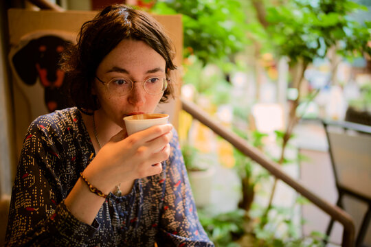 Young woman with glasses drinks coffee in a cozy, leafy cafe setting. Chengdu, Sichuan, China