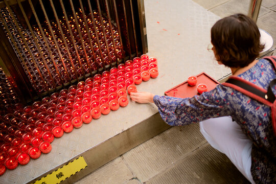 Woman arranging red tea light candles on a metal step in an outdoor setting. Chengdu, Sichuan, China