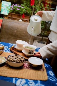 Person pours tea into bowls on a table with snacks and colorful cloth settings. Chengdu, Sichuan, China