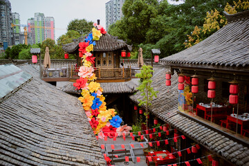 Vibrant floral display flows down traditional architecture amidst lush greenery and urban backdrop. Chengdu, Sichuan, China