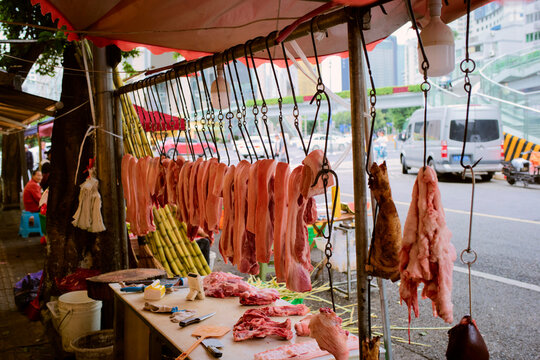 Fresh meat hangs from hooks at an outdoor market stall on a busy street. Chengdu, Sichuan, China