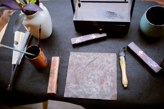 Art supplies on a black tablecloth including brushes, ink stones, and a ceramic vase. Chengdu, Sichuan, China