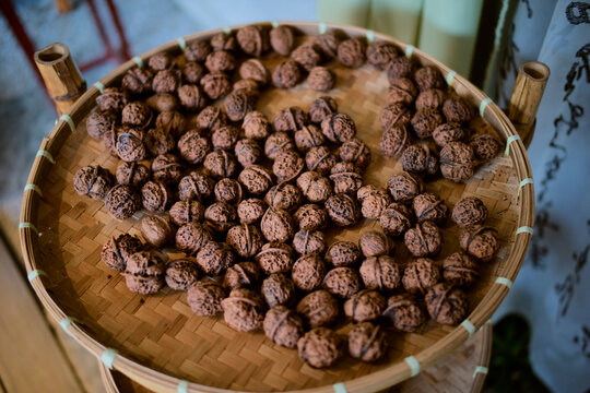 A woven basket filled with whole walnuts on a wooden surface. Chengdu, Sichuan, China