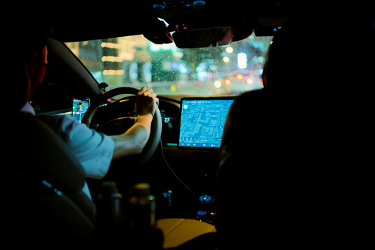 Driver holding steering wheel in a car at night with illuminated GPS screen in urban setting. Chengdu, Sichuan, China